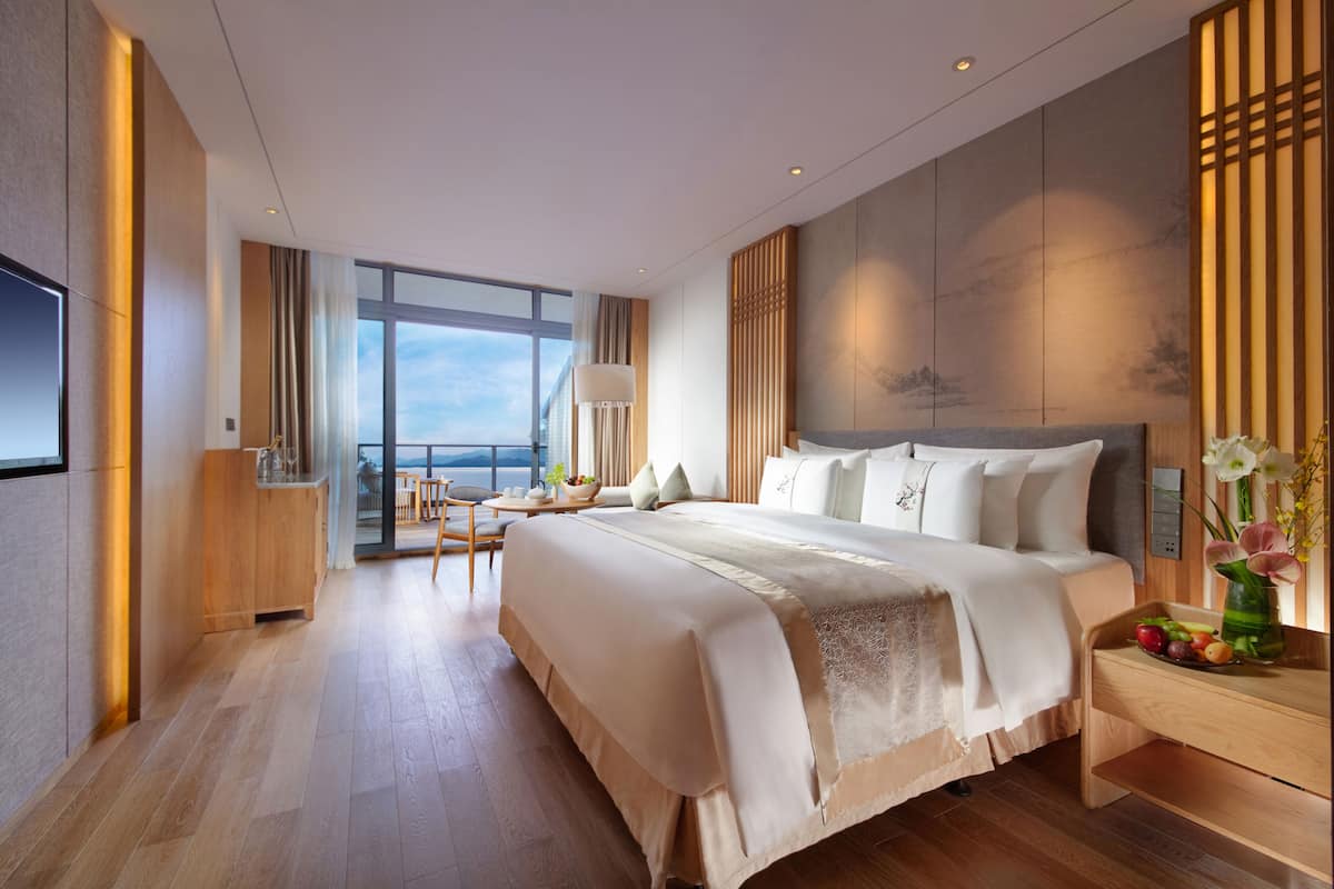 A modern hotel room with a large bed, a desk, and a view of the ocean.