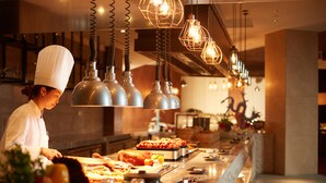 A chef preparing food in a well-lit kitchen with modern pendant lights and a variety of dishes displayed on the counter. - Bright QiandaoLake Resort (Hangzhou)