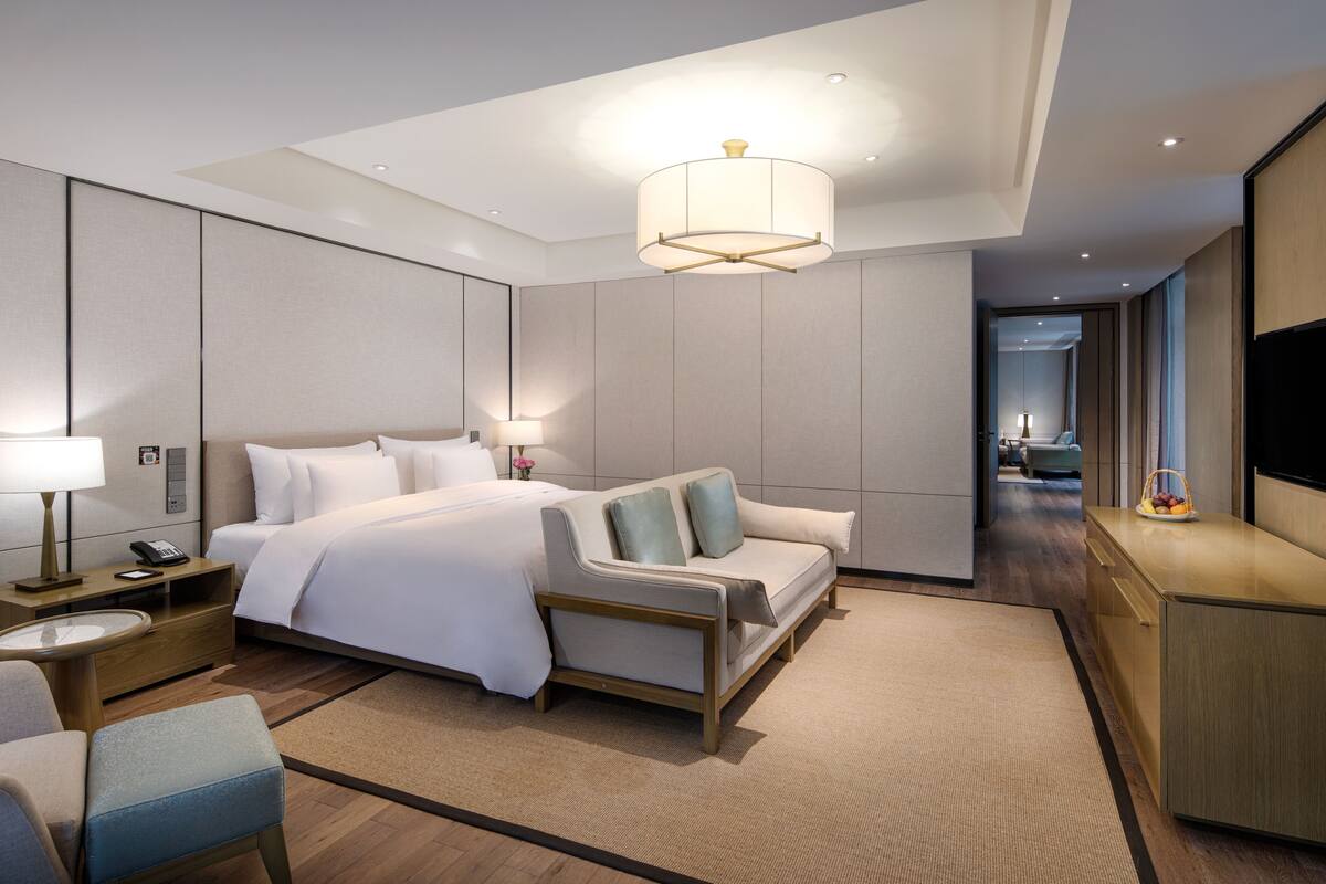 A modern hotel room with a large bed, a sofa, a desk, and a TV.