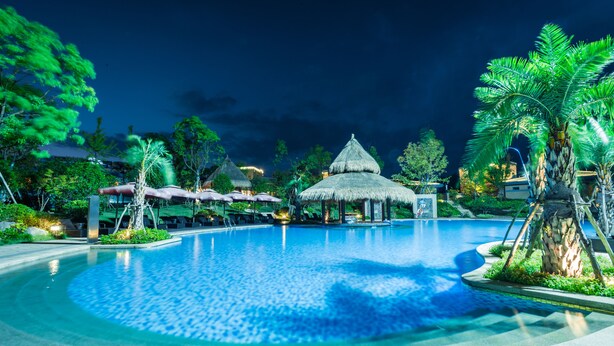 A large, clear swimming pool with a thatched-roof pavilion in the center, surrounded by palm trees and lounge areas. - Bright QiandaoLake Resort (Hangzhou)
