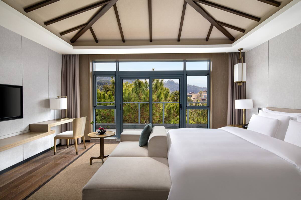 A modern hotel room with a large bed, a desk, a chair, and a TV.