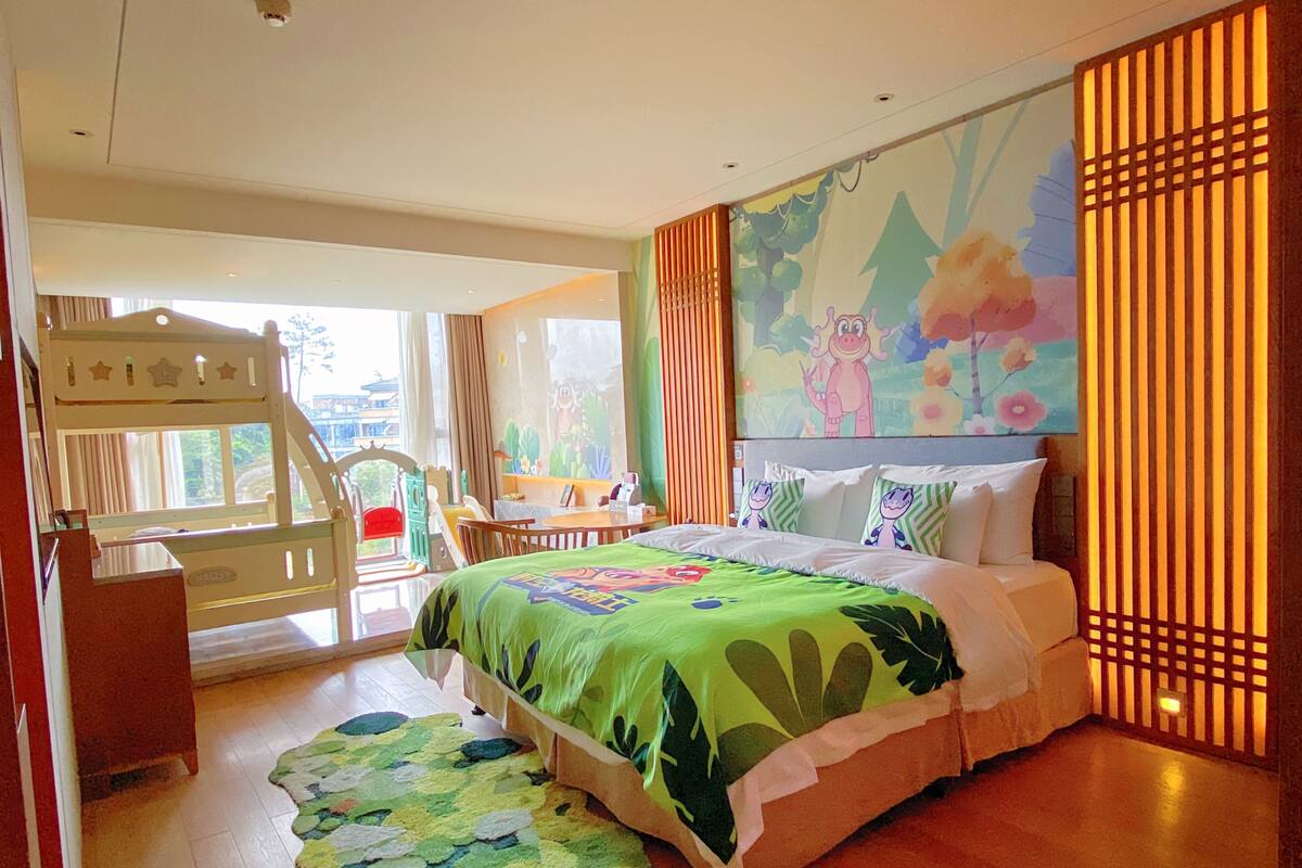 A child-friendly hotel room with a bunk bed, a desk, and a large window.