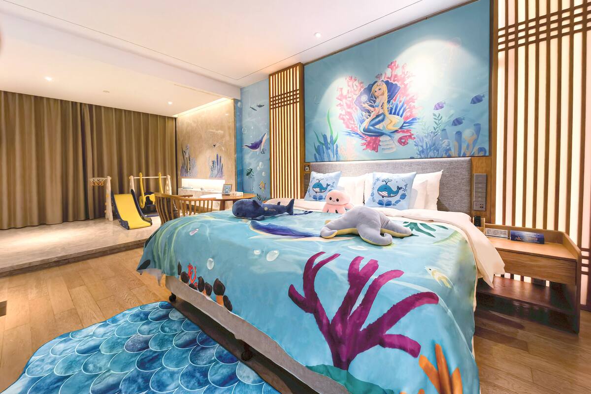 A bedroom with an underwater theme, featuring a bed with a blue and purple coral design, a wooden headboard, and a small desk with a chair.