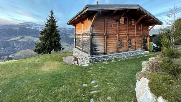 Eine Holzhütte mit steinernen Fundamenten vor einer Bergkulisse.