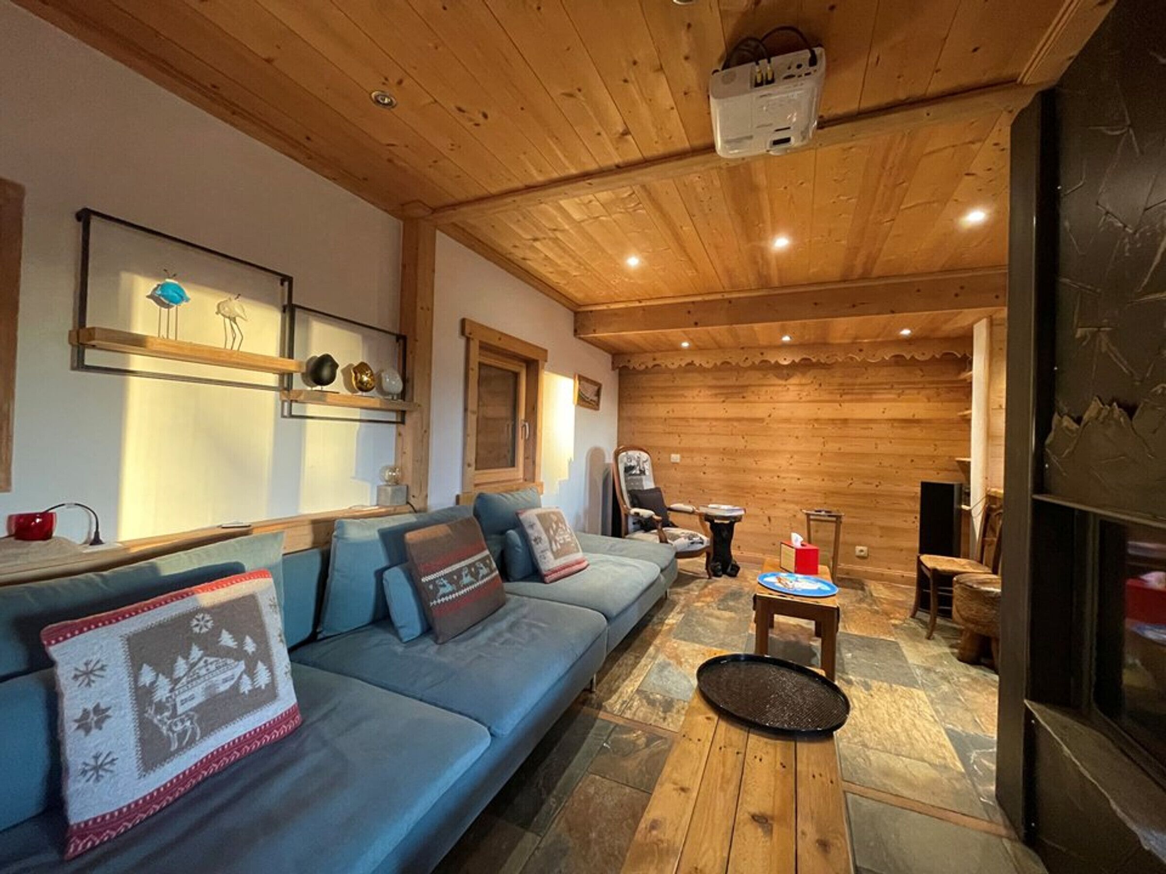 A cozy log cabin interior with a blue sofa, wooden flooring, and a projector mounted on the ceiling.