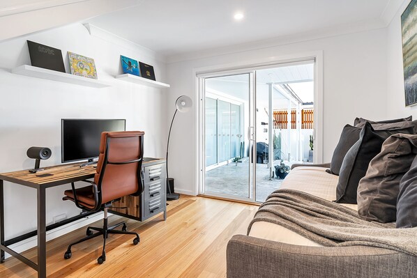 A modern living room with a desk, a comfortable sofa, and a large window. - White Water - Stunning Ocean View w/ Private Pool (Kiama)
