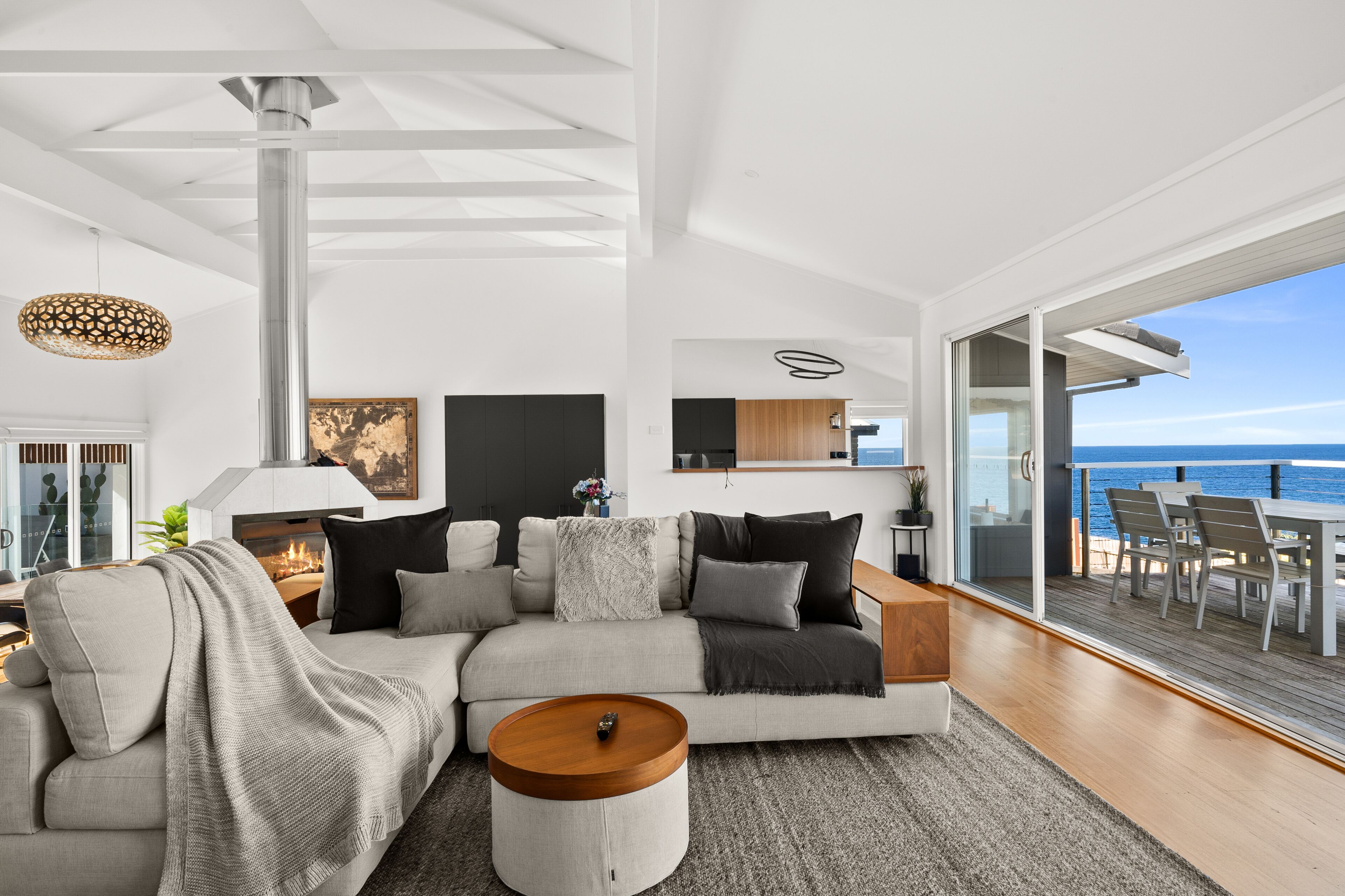 A modern living room with a large sectional sofa, a round coffee table, and a view of the ocean through large sliding glass doors.