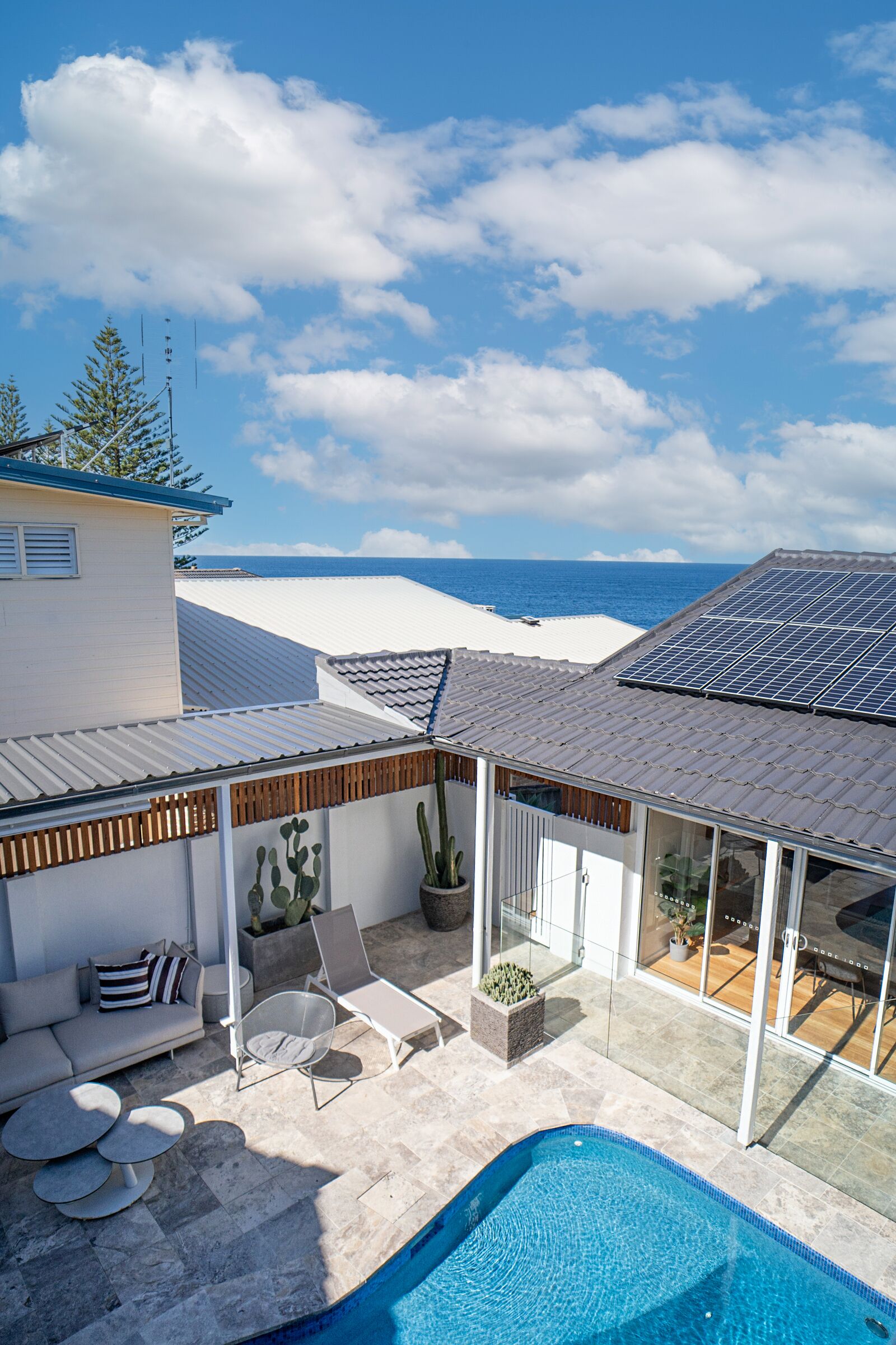A modern outdoor pool area with a view of the ocean, a covered seating area, and a solar panel roof.