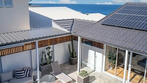Un espace piscine extérieur moderne avec vue sur l’océan, un coin salon abrité et un toit équipé de panneaux solaires.