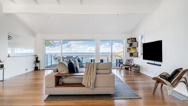 Un vaste salon doté d’une grande fenêtre donnant sur la mer, d’un téléviseur à écran plat fixé au mur et d’un coin salon confortable avec un canapé et des fauteuils.
