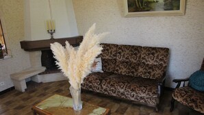 A living room with a patterned sofa, a small table with a vase of pampas grass, a bench, and a painting on the wall.