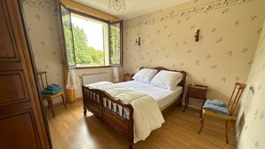 A bedroom with a wooden bed, a radiator, a window with curtains, and a floral wallpaper pattern.