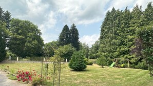 A well-maintained garden with a swing set, a small pond, and a variety of trees.