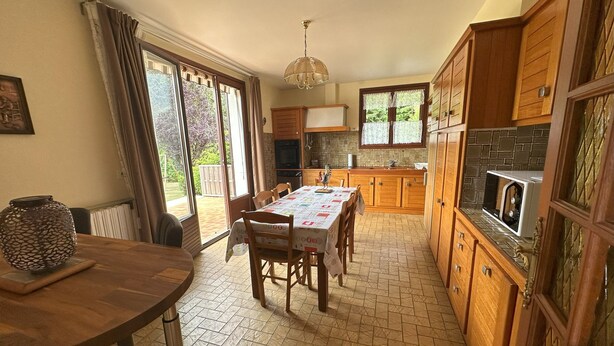 A kitchen with wooden cabinets, a dining table with chairs, and a large window with curtains.