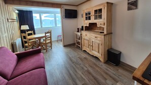 Un accogliente soggiorno con pavimento in legno, un divano rosso, un tavolo da pranzo con sedie, un mobile contenitore in legno e un televisore a parete.