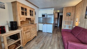 Un ambiente compatto con angolo cottura, mobili in legno, un divano rosso e un piccolo tavolo da pranzo.
