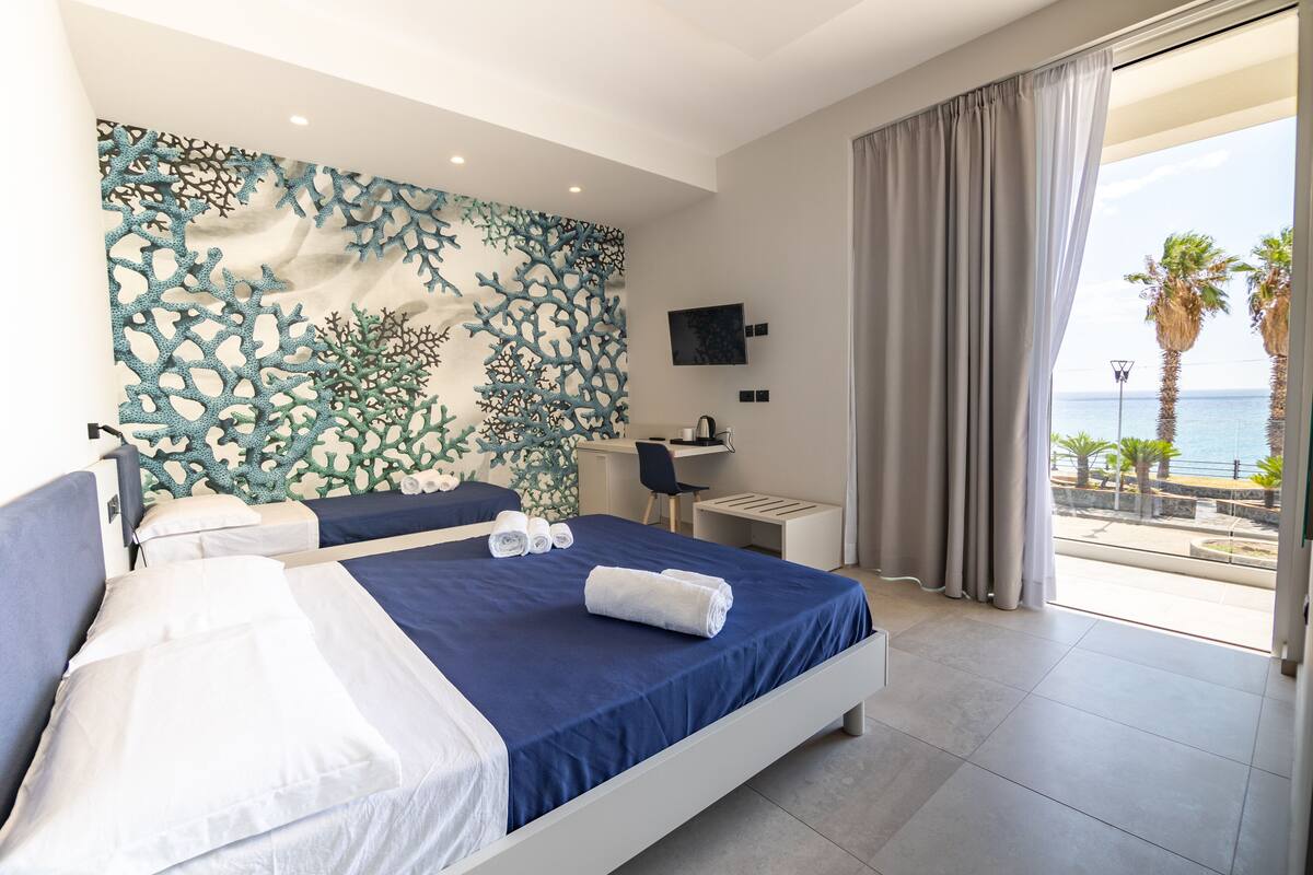 A bedroom with a bed, a desk, and a view of the sea.