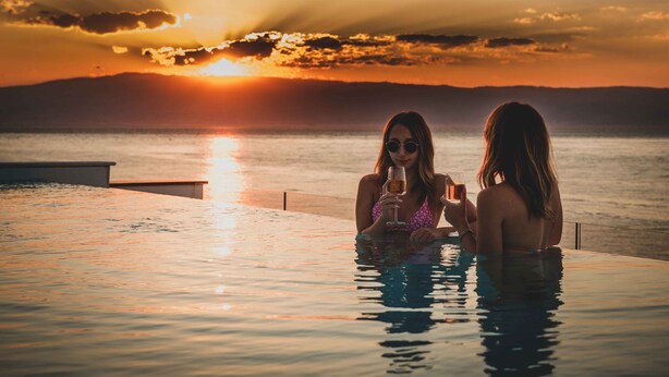 Dos personas en una piscina con vista al atardecer.