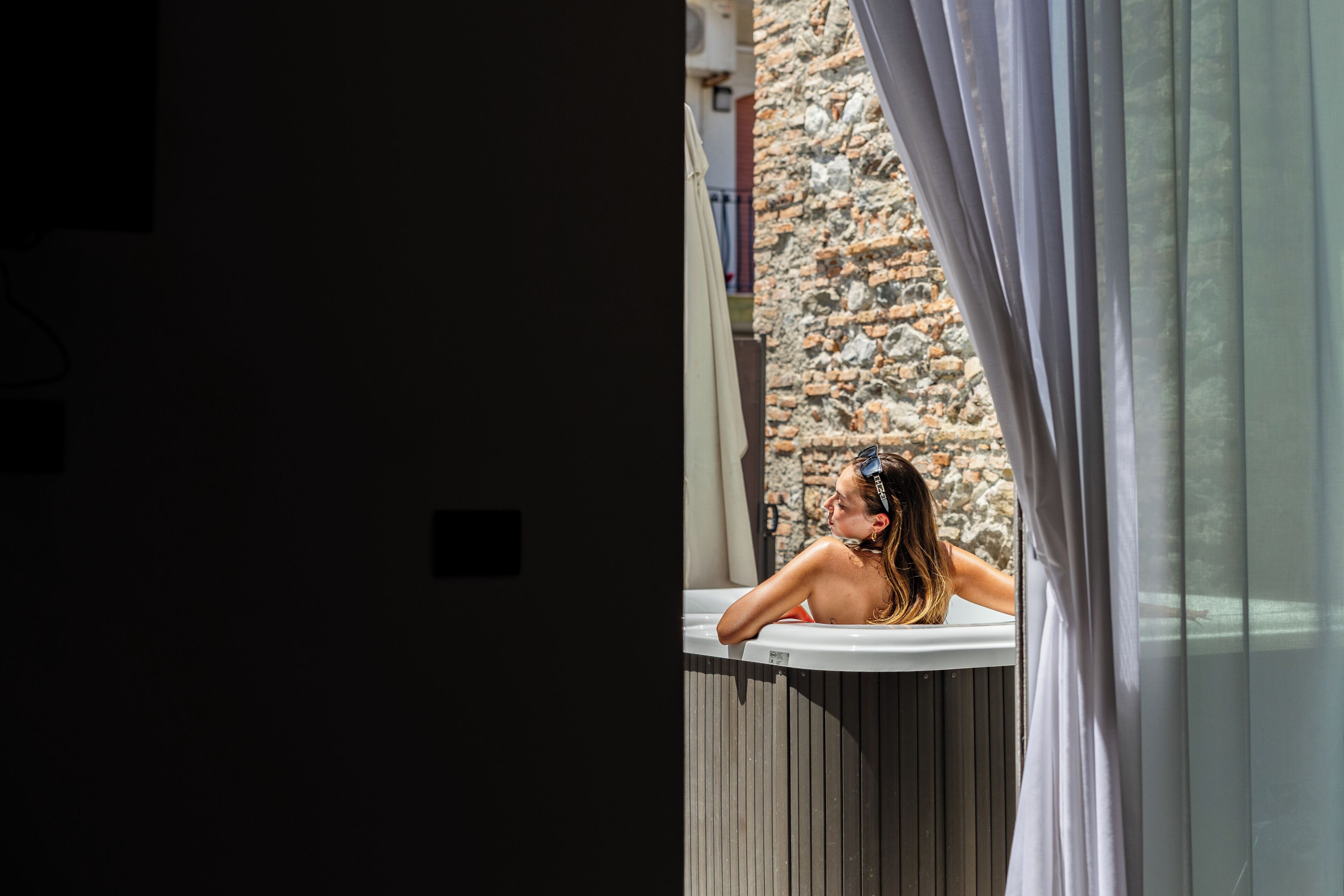 Une personne dans une baignoire, avec un mur en pierre et une fenêtre en arrière-plan.