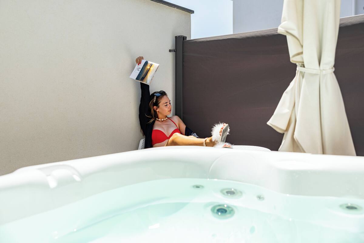 A person relaxing in a hot tub with a book, a towel, and a robe.