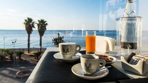 Preparación para el desayuno con vista al océano, que incluye una taza de café, jugo y una botella de agua sobre una mesa.