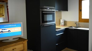 A compact kitchen with a black refrigerator, a built-in oven, and a coffee maker. - Cozy 1-Bedroom Apartment, Well-Equipped, Near Ski Slopes and Village Center (Crest-Voland)