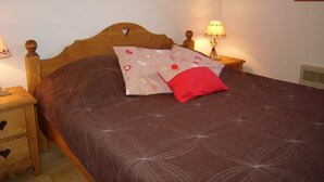 A neatly made bed with a patterned bedspread, a red pillow, and a bedside lamp on a wooden nightstand. - Cozy 1-Bedroom Apartment, Well-Equipped, Near Ski Slopes and Village Center (Crest-Voland)