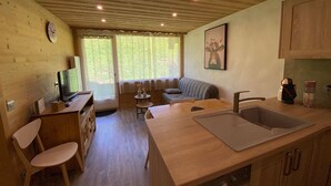 Una cocina compacta con un lavamanos, armarios de madera, una zona de comedor con mesa y sillas, y un televisor sobre un mueble de madera.