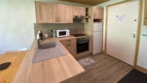 Una cocina compacta con gabinetes de madera, microondas, estufa y refrigerador.