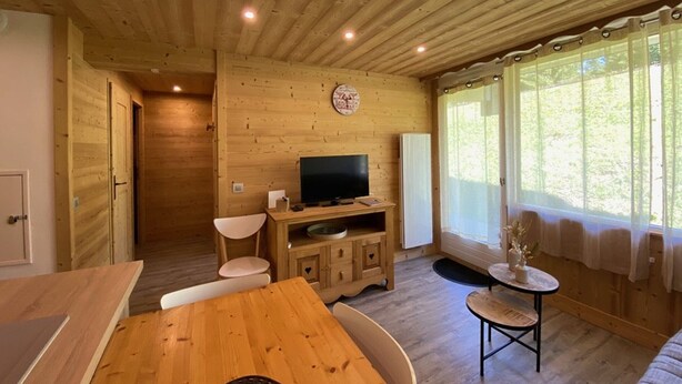 Un interior de madera con una mesa de comedor, sillas, un televisor y una ventana con cortinas.