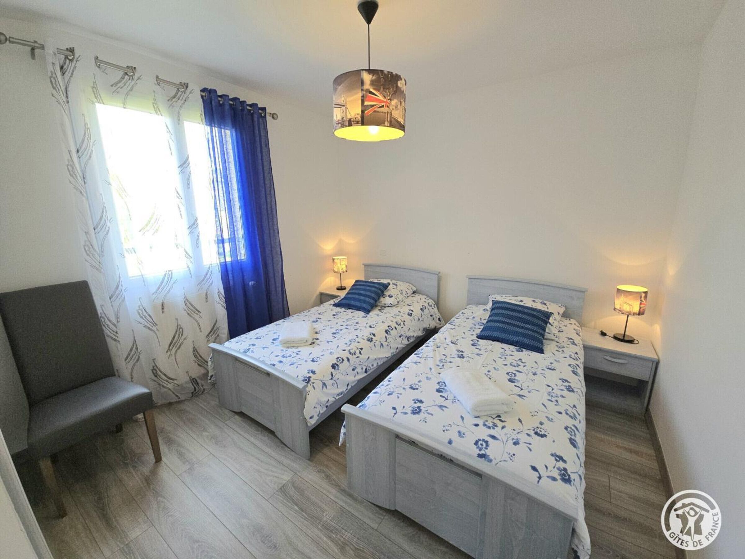 Quarto com duas camas, uma cadeira e um lustre.