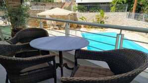 Un balcon doté de meubles en osier, d’une table et offrant une vue sur une piscine.