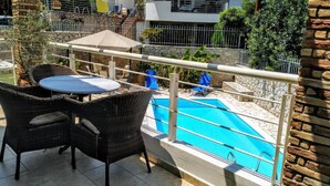 Un balcon avec une piscine, des meubles en osier et un mur en pierre.