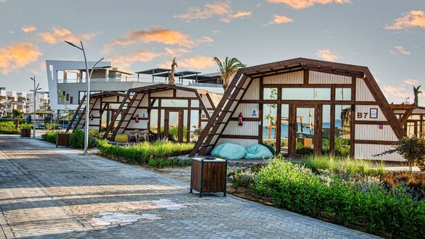 Un hôtel situé en bord de mer, doté de cabanes en bois, d’une promenade dallée et offrant une vue sur la mer.