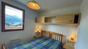 Ett sovrum med en säng, två sängbord med lampor, ett fönster med utsikt över bergen och en hängande taklampa.