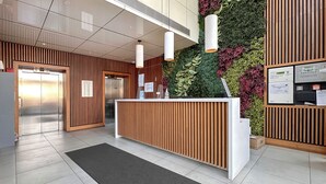 Un espace d’accueil moderne, doté d’un comptoir de réception en bois, d’un jardin vertical verdoyant et d’un panneau d’affichage numérique.