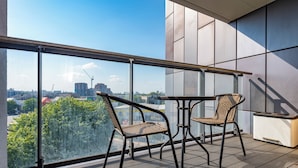 Un balcon avec deux fauteuils en osier, une petite table et un chauffage encastré. On peut admirer la vue sur la ville à travers les grandes fenêtres.