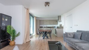 Un salon moderne avec un canapé gris, une table basse noire et un coin repas comprenant une table et des chaises en bois.