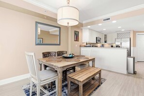 A dining area with a wooden table, white chairs, a bench, and a chandelier. - South Beach Boardwalk Condo (Ocean City)