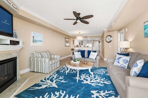 A living room with a fireplace, striped armchair, round coffee table, and a blue coral-patterned rug. - South Beach Boardwalk Condo (Ocean City)