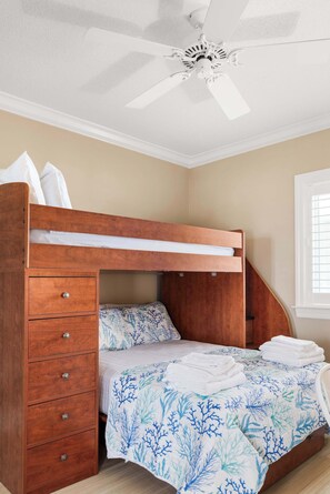A bunk bed with a wooden headboard and drawers, a ceiling fan, and a window with blinds.