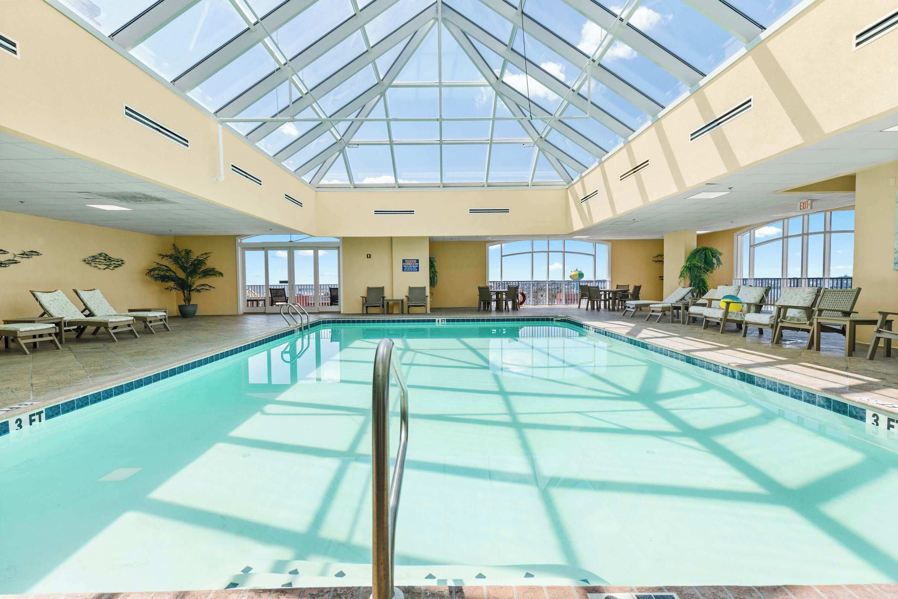 A large indoor swimming pool with a glass ceiling, lounge chairs, and a view of the sky.