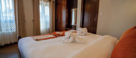 A neatly made bed with towels, a tray, and a gift in a hotel room with wooden furniture and a large mirror.