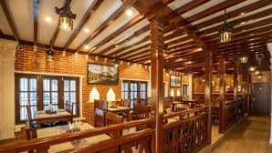 A restaurant with brick walls, wooden beams, and multiple dining tables and chairs. - Airport Himalaya Boutique Hotel (Kathmandu)