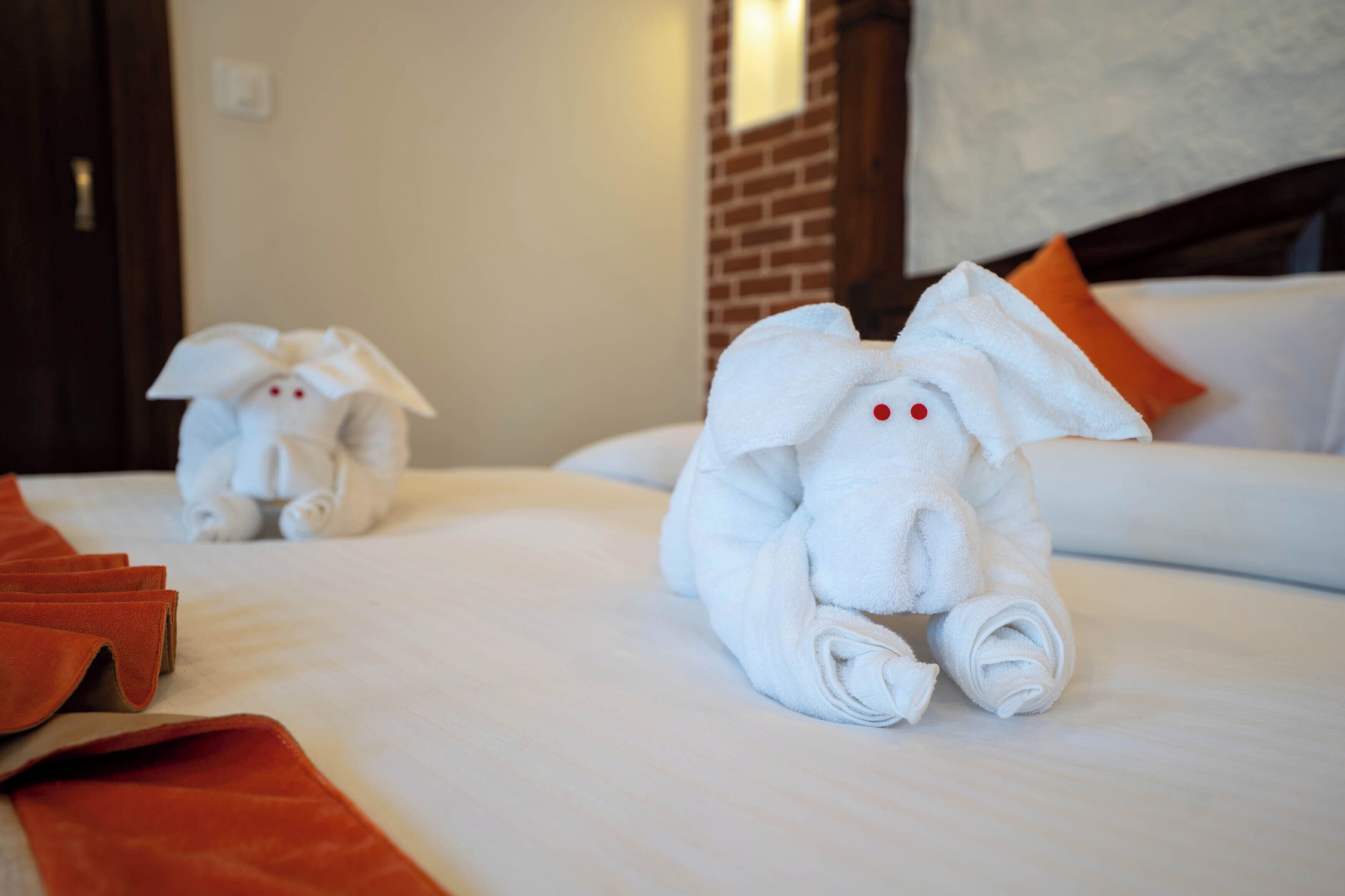 Habitación de hotel con una cama bien hecha, una pared de ladrillo y un sofá blanco con almohadas anaranjadas.