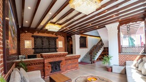 A spacious lobby with a brick fireplace, wooden ceiling beams, and a staircase leading to upper floors. - Airport Himalaya Boutique Hotel (Kathmandu)