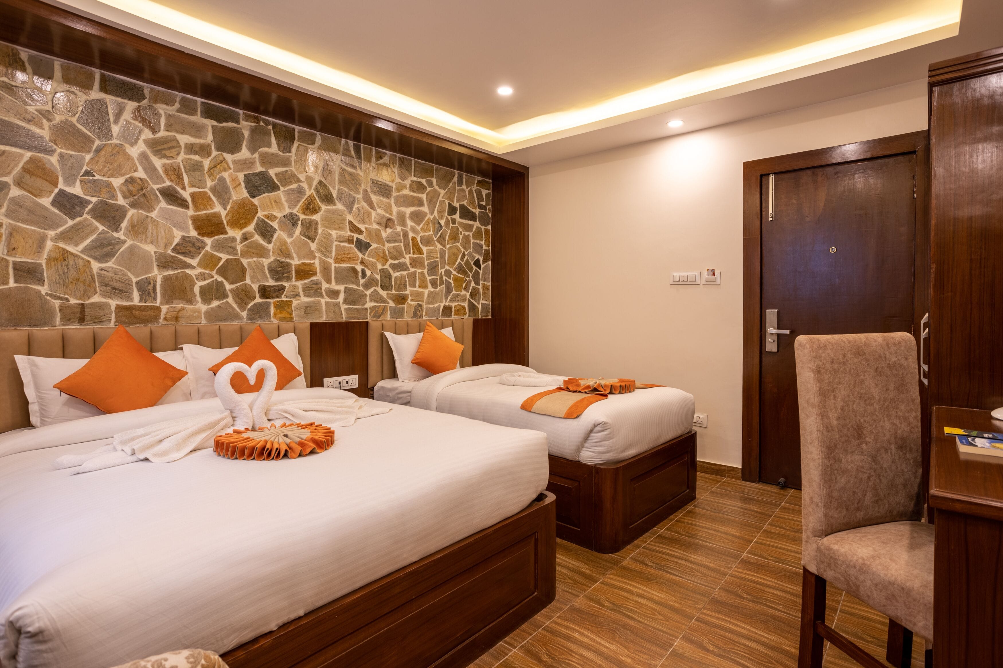 Habitación de hotel con dos camas, una pared de piedra, una puerta de madera y una pequeña mesa con una silla.