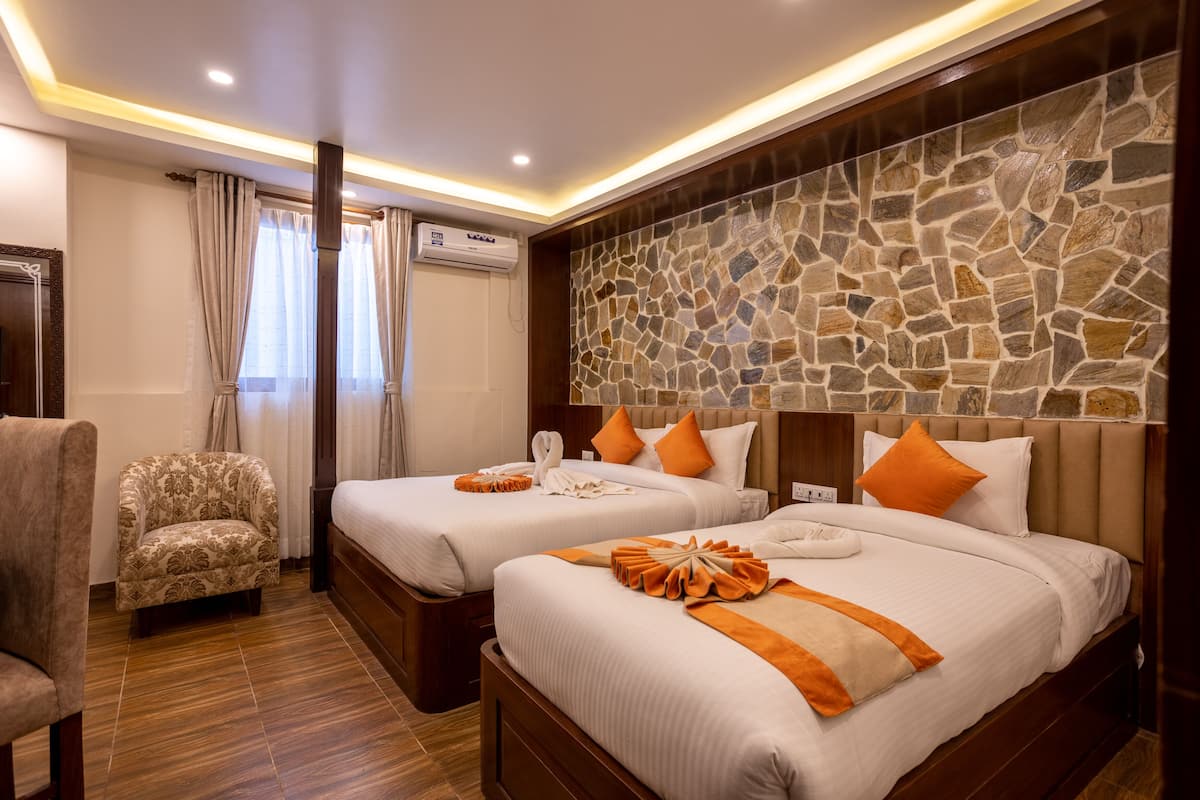 A hotel room with two beds, a chair, a stone wall, and an air conditioning unit.