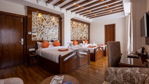A hotel room with two wooden beds, a stone wall, a wooden ceiling, a dining table, and a television. - Airport Himalaya Boutique Hotel (Kathmandu)