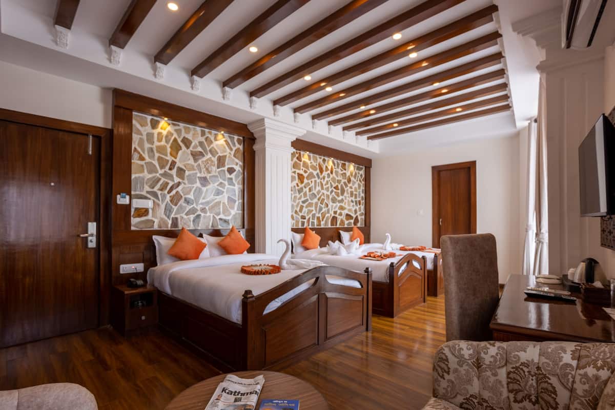 A hotel room with two wooden beds, a stone wall, a wooden ceiling, a dining table, and a television.